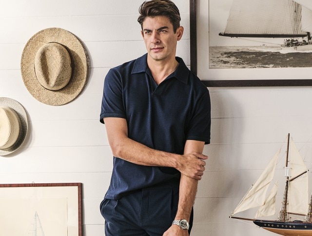 Ein Mann mit einem dunkelblauen Polo und einer dunkelblauen Hose steht in einem maritivem Raum.