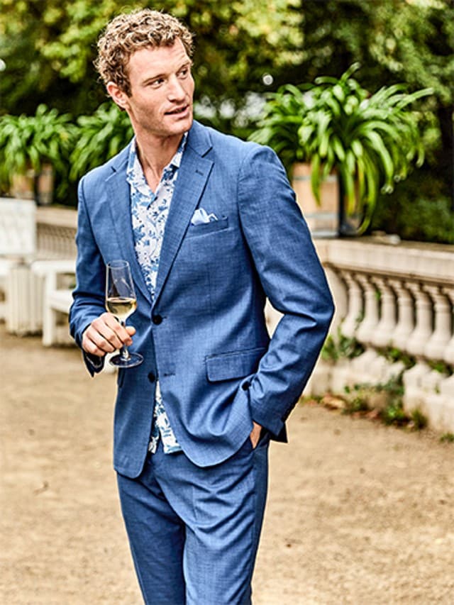 Mann trägt einen blauen Anzug und hält ein Glas Sekt in der Hand