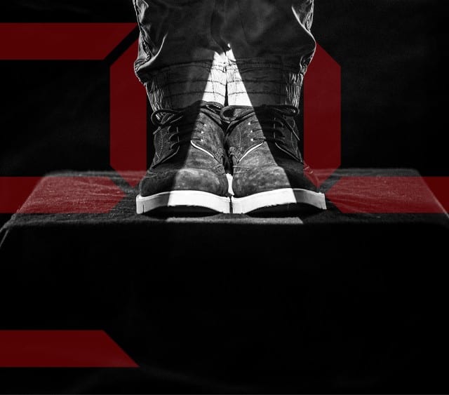 Auf dem Bild stehen ein Paar Schuhe auf einem Podest, umgeben von Rauch, während im Hintergrund große rote, digital wirkende SALE‑Zahlen leuchten.