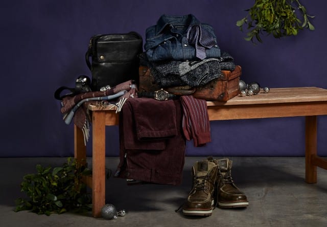 Das Bild zeigt ein stilvoll arrangiertes Ensemble aus Herrenbekleidung und Accessoires auf einer Holzbank vor festlicher Kulisse.