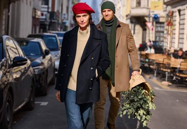 Das Bild zeigt zwei modisch gekleidete Personen, die an einem sonnigen Tag durch eine Stadtstraße spazieren.