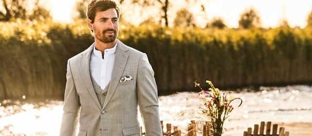 Ein Mann im Hochzeitsanzug vor einem See mit Sonne.