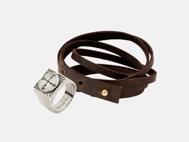 Das Bild zeigt ein Accessoire-Set bestehend aus einem silberfarbenen Ring mit Kompassgravur und einem mehrfach gewickelten, braunen Lederarmband mit Metallschließe.