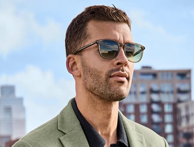 Ein Mann trägt eine dunkle Sonnenbrille, ein schwarzen Poloshirt und ein hellgrünes Sakko.