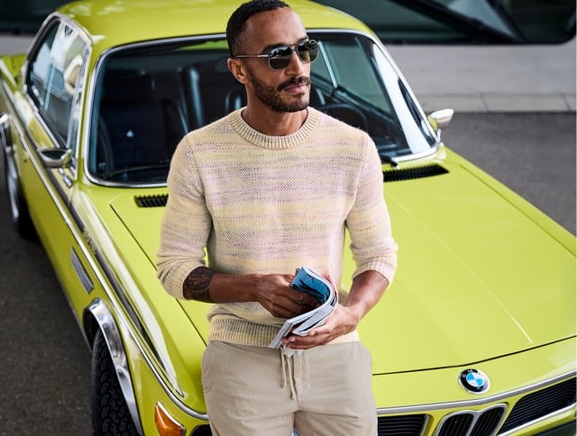 Ein Mann trägt einen hellen, pastellfarben melierten Strickpullover und eine beige Hose.