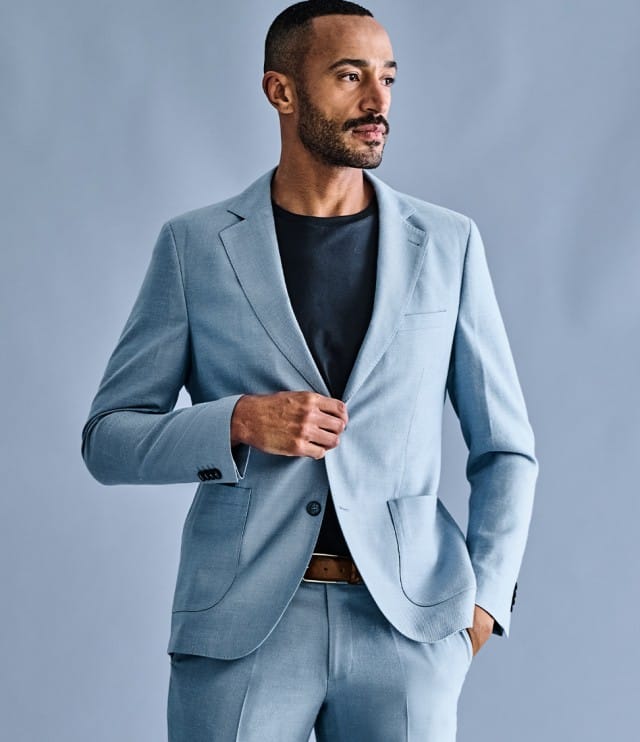 Ein Mann trägt einen hellblauen Anzug mit passendem Sakko und Hose, kombiniert mit einem schwarzen T‑Shirt und einem braunen Gürtel.