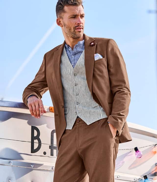 Ein Mann trägt einen hellbraunen Anzug mit passender Weste und Hoseund steht an einer Outdoorbar.