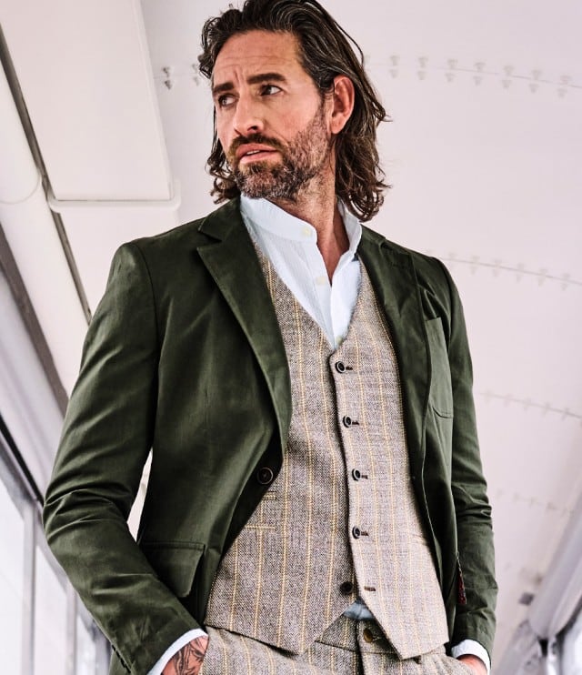 Ein Mann trägt ein grünes Sakko über einer hellgrauen Weste.