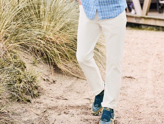 Zu sehen sind weiße Sommerhosen kombiniert mit Sneakern und einem blau kariertem Hemd.