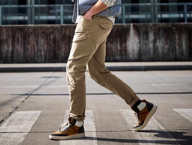 Ein Mann geht über einen Zebrastreifen und trägt eine beige Cargohose kombiniert mit zweifarbigen High-Top-Sneakern in Braun, Weiß und Schwarz.