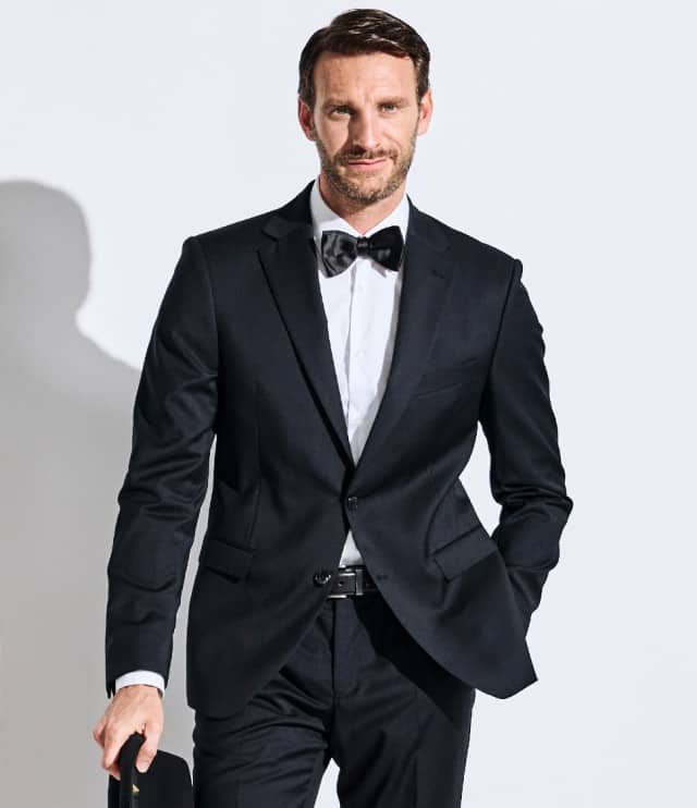 Der Mann trägt einen klassisch-eleganten schwarzen Anzug mit weißem Hemd und schwarzer Fliege – ein stilvoller Look für besondere Anlässe.