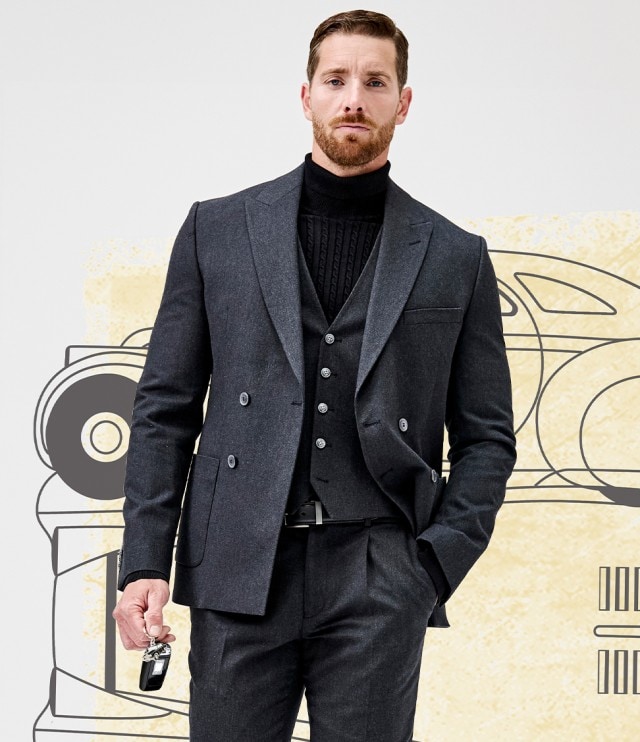 Ein Mann trägt einen eleganten dunkelgrauen Anzug mit Weste und schwarzem Rollkragenpullover, hält in einer Hand einen Autoschlüssel und steckt die andere Hand lässig in die Hosentasche.