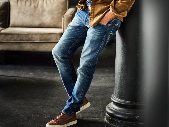 Der Look zeigt eine klassische, schmal geschnittene Bluejeans kombiniert mit braunen Ledersneakern und einer hellbraunen Cordjacke – ein lässig-zeitloses Outfit mit modernem Casual-Charme.