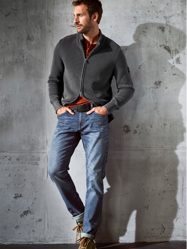 Smart Casual gekleideter Mann der an einer Steinwand lehnt