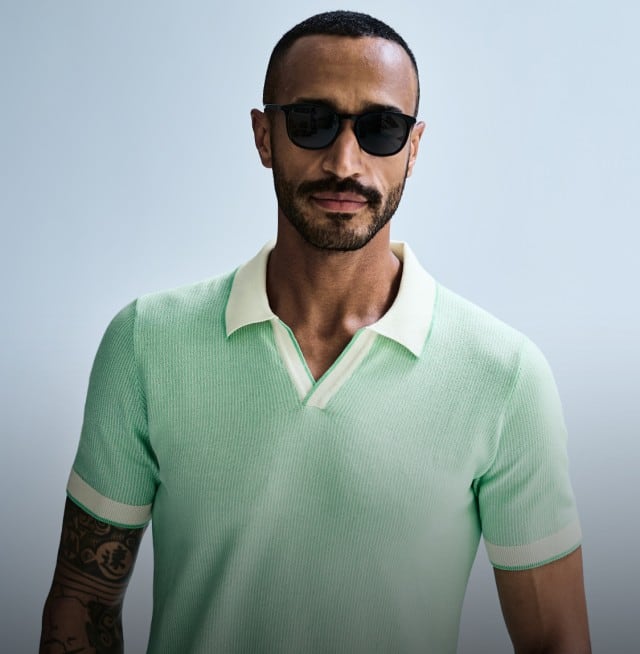 Ein Mann trägt ein mintfarbenes Poloshirt und eine dunkle Sonnenbrille und blickt frontal in die Kamera.