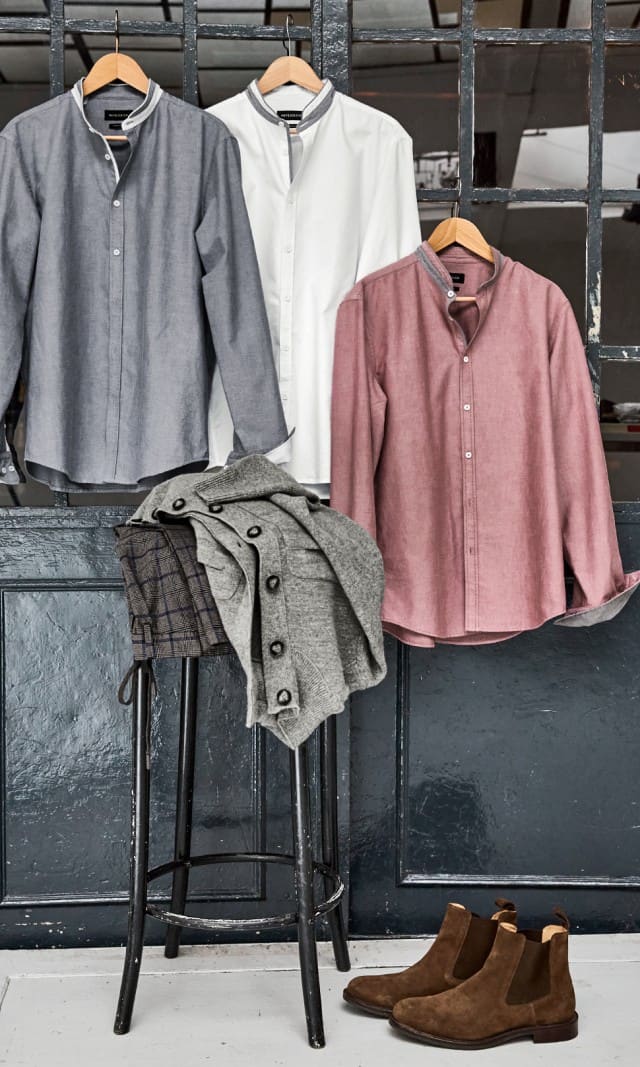 Drei Hemden in den Farben grau, weiß und rot hängen an einr Industrietür, darunter steht ein Hocker auf dem weitere Bekleidungsstücke liegen.