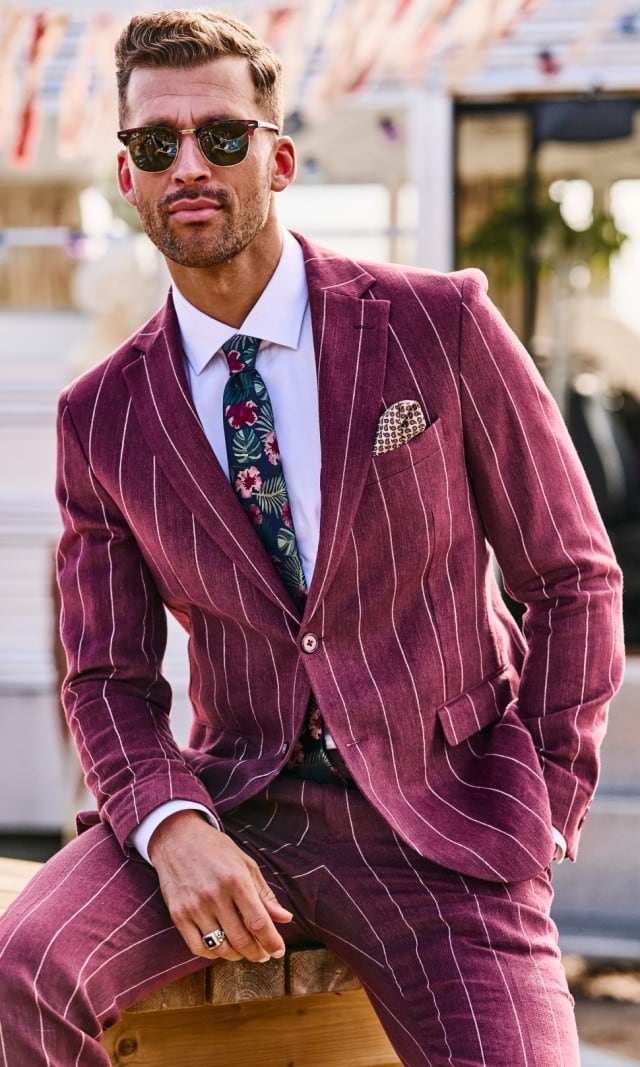 Ein Mann in einem roten Nadelstreifenanzug und einer Sonnenbrille sitzt lässig auf einem Hocker.