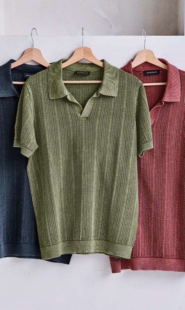 Drei Polohemden hängen auf einem Holzbügel an einer Wand.