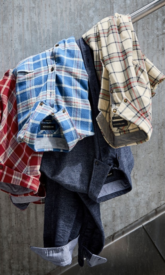 Über einem Trepppengeländer hängen drei verschiedene Flanellhemden und ein Jeanshemd.