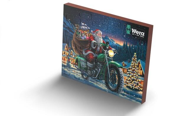 Auf dem Bild ist ein Wera-Adventskalender zu sehen, der eine weihnachtliche Illustration von Santa Claus auf einem grünen Motorrad vor einer verschneiten Dorflandschaft zeigt.