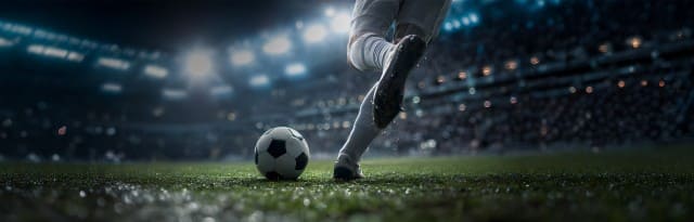 Ein Fußballspieler in weißer Sportkleidung trifft auf einem beleuchteten Stadionrasen einen Ball, während im Hintergrund ein ausverkauftes Stadion mit Flutlicht zu sehen ist. Ein Fußballspieler in weißer Sportkleidung trifft auf einem beleuchteten Stadionrasen einen Ball, während im Hintergrund ein ausverkauftes Stadion mit Flutlicht zu sehen ist.