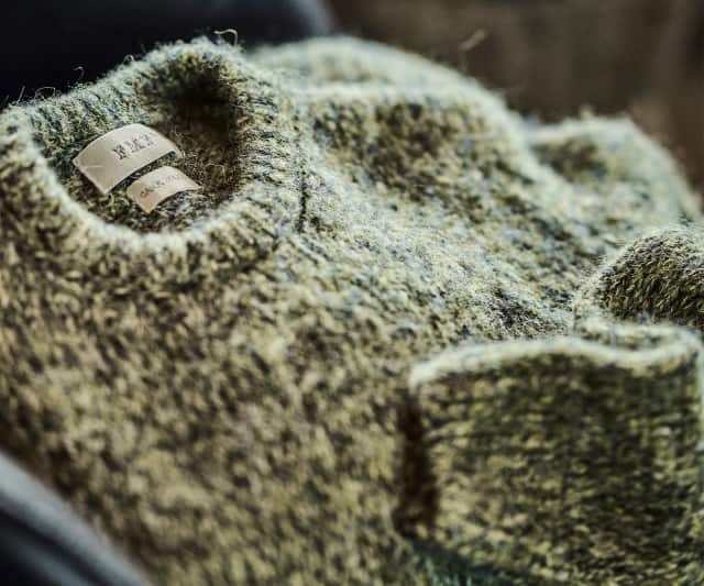 Auf dem Bild ist ein nah aufgenommener, flauschiger Strickpullover in melierter Optik mit sichtbarem Etikett zu sehen.
