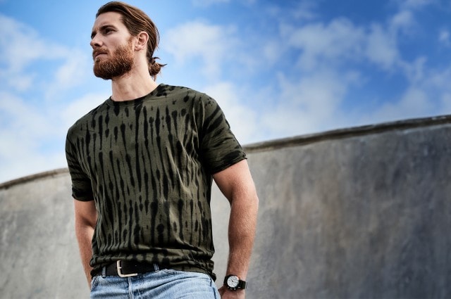 Mann in einem grün gemusterten T-Shirt und Jeans der nach links in die Ferne schaut
