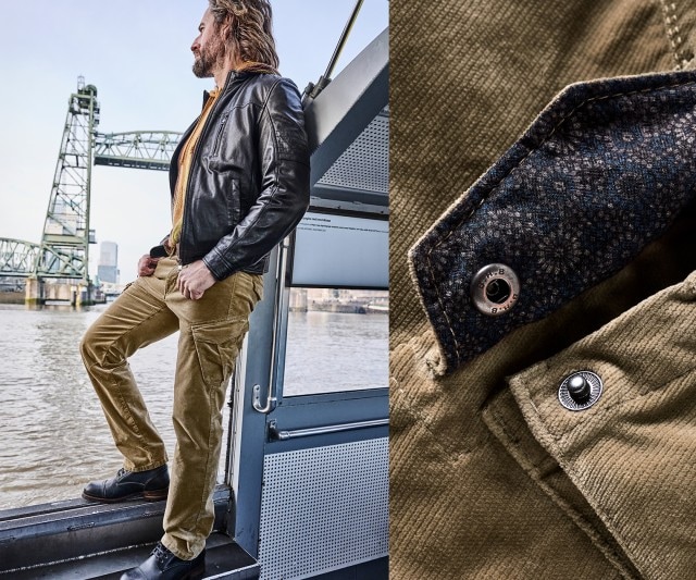 Ein Mann trägt eine schwarze Lederjacke über einem senfgelben Oberteil und kombiniert dazu eine sandfarbene Cordhose mit Cargotaschen und schwarzen Schnürschuhen.