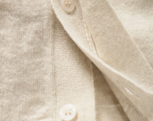 Auf dem Bild ist eine Nahaufnahme eines beigen Kaschmirstrickstoffs mit Knopfleistendetails und zwei hellen Knöpfen zu sehen.