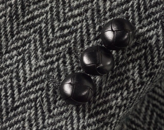 avatar Auf dem Bild ist eine Nahaufnahme eines grau‑schwarzen Fischgrätstoffs mit drei dunklen, geflochten wirkenden Lederknöpfen zu sehen. avatar Auf dem Bild ist eine Nahaufnahme eines grau‑schwarzen Fischgrätstoffs mit drei dunklen, geflochten wirkenden Lederknöpfen zu sehen.