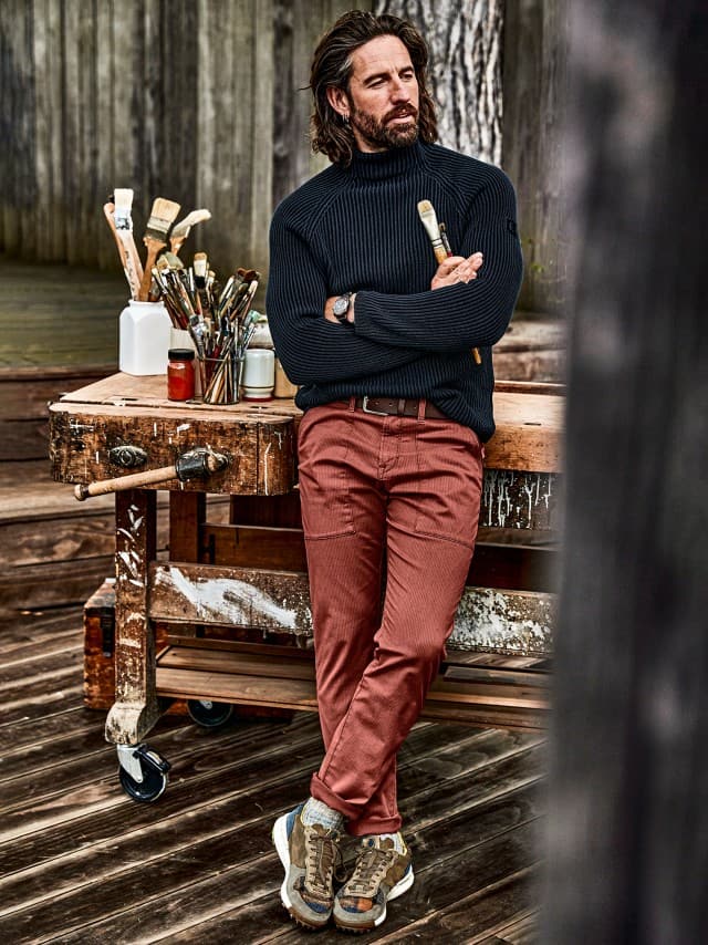 Ein Mann trägt eine dunkelblaue Jacke über einem blauen Hemd mit gelbem T-Shirt, dazu beige Cargohosen und braune Wildlederschuhe – ein lässiger, stilvoller Freizeitlook.