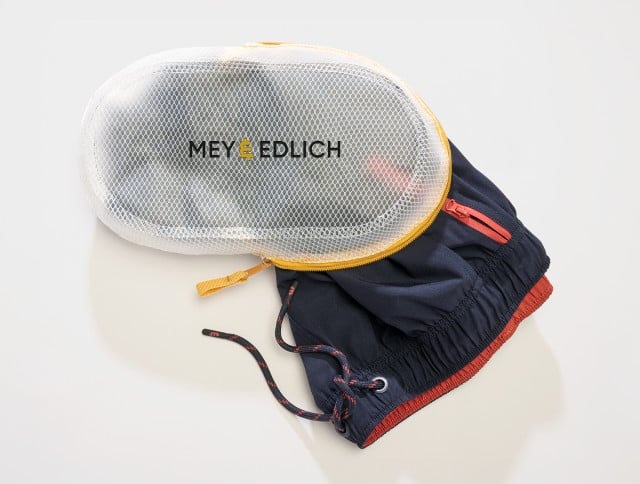 Auf dem Bild ist ein Paar zusammengefalteter Shorts zu sehen, das teilweise in einer weißen Netz‑Reißverschlusstasche mit dem Aufdruck „MEY & EDLICH“ steckt.