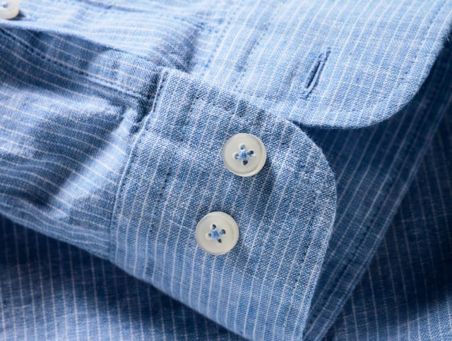 Das Bild zeigt eine Detailaufnahme von einem blauen Hemd mit feinen weißen Streifen.