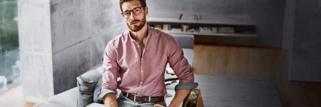 Ein Mann trägt ein rosafarbenes Hemd mit Stehkragen, hochgekrempelten Ärmeln und einem braunen Gürtel.