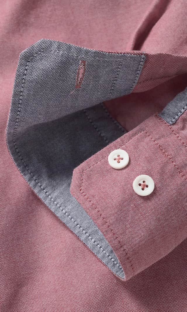 Der Mann trägt ein rosafarbenes Stehkragenhemd mit hochgekrempelten Ärmeln sowie eine hellgraue Jeans.