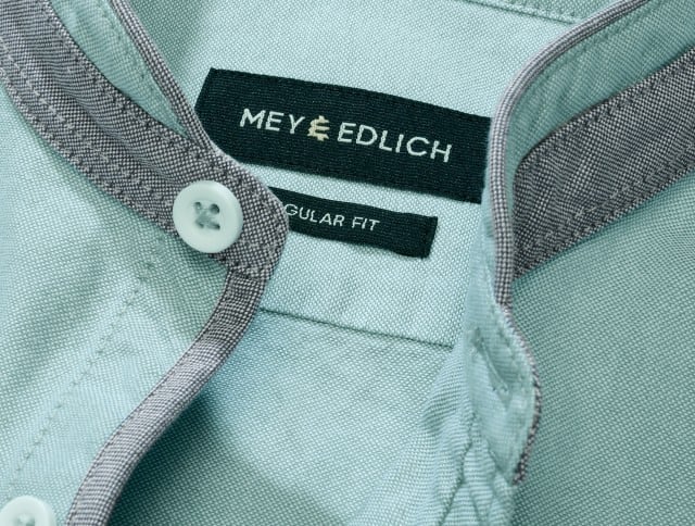 Auf dem Bild ist der Kragenbereich eines mintgrünen Hemds mit grauer Innenpaspel und sichtbarem Markenlabel „MEY & EDLICH“ sowie dem Zusatz „REGULAR FIT“ zu sehen.