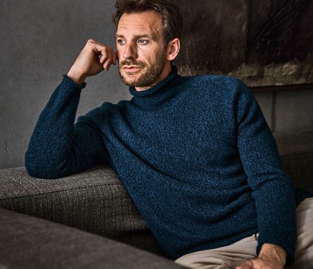 Ein Mann trägt einen dunkelblauen Rollkragenpullover aus grobem Strick, der auf der rechten Seite des Bildes auch einzeln abgebildet ist.