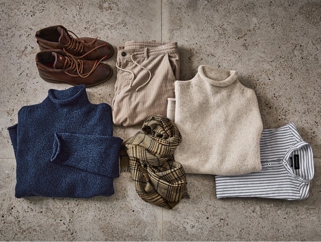 Auf dem Bild sind herbstlich-winterliche Kleidungsstücke und Accessoires zu sehen, darunter braune Stiefel, eine beige Hose, zwei Rollkragenpullover (blau und beige), ein gestreiftes Shirt und ein kariertes Tuch.
