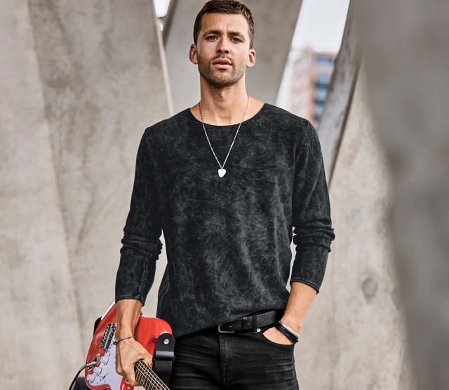 Mann sitzt im Freien und trägt einen blauen Strickpullover mit strukturierter Oberfläche und eine dunkle Hose; rechts daneben ist derselbe blaue Pullover als Produktaufnahme zu sehen.