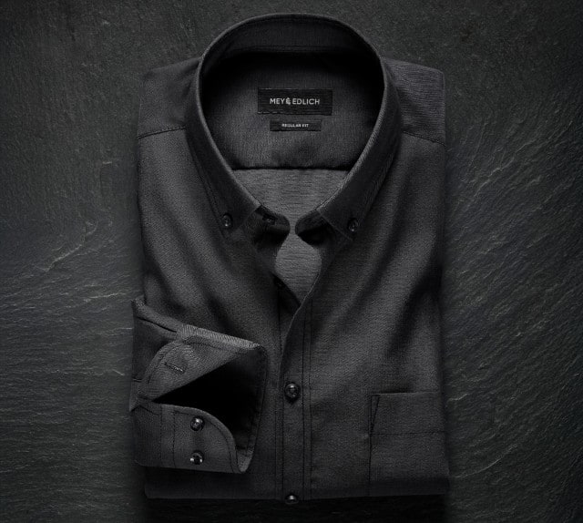 Das Bild zeigt ein schwarzes Stehkragenhemd von Mey & Edlich in Regular Fit mit feiner Struktur und glänzender Oberfläche, stilvoll auf dunklem Untergrund arrangiert.