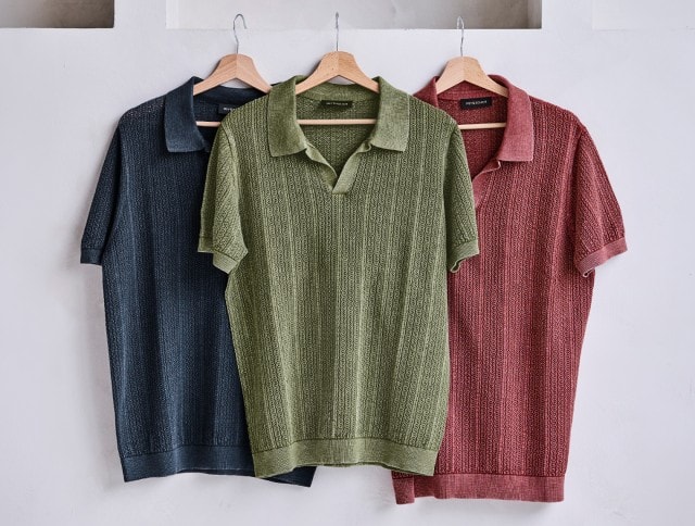 An einer Wand hängen drei Strick Polos jeweils auf einem Holzkleiderbügel