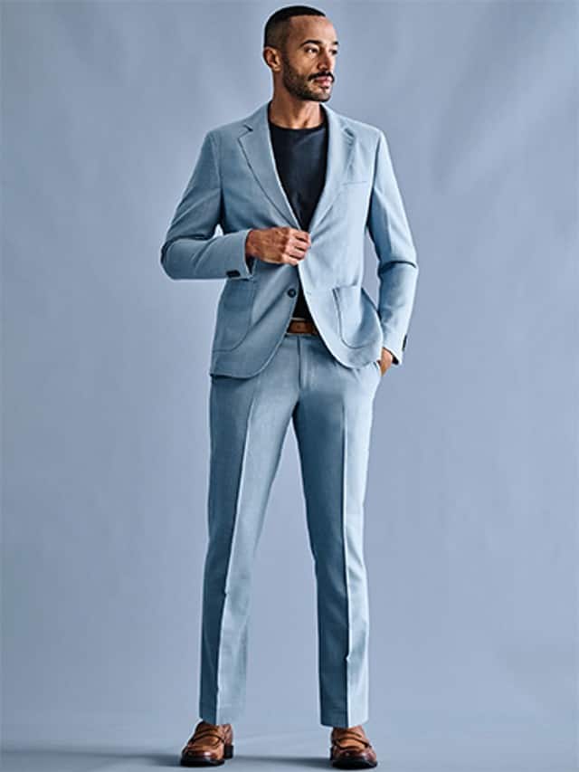 Ein Mann trägt einen hellblauen Anzug mit passendem Sakko und Hose, kombiniert mit einem schwarzen T‑Shirt, braunem Gürtel und braunen Schuhen.
