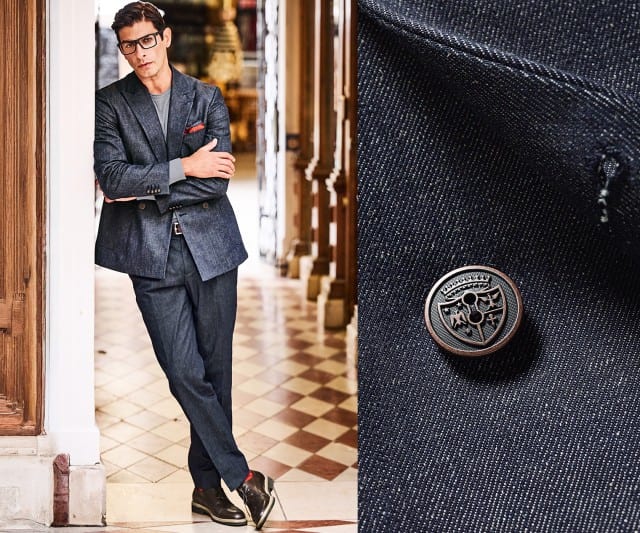 avatar Ein Mann trägt einen dunkelblauen Anzug und lehnt lässig an einer Säule, während rechts eine Nahaufnahme eines Knopfes seines Jackets zu sehen ist.