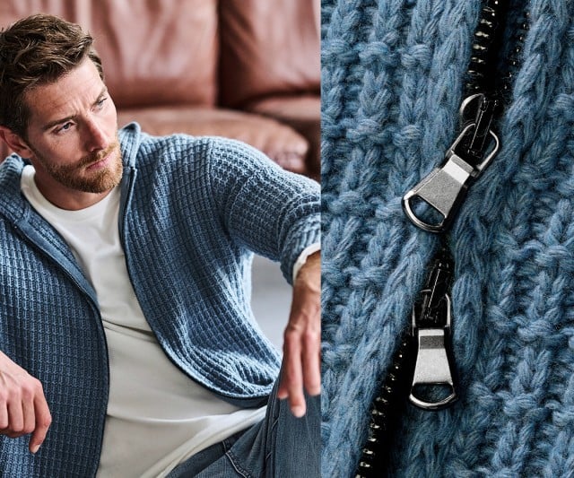 Ein Mann sitzt entspannt auf einem Sofa und trägt eine grob gestrickte blaue Kapuzenjacke über einem weißen T‑Shirt, während rechts ein Nahdetail des Jackenreißverschlusses zu sehen ist.