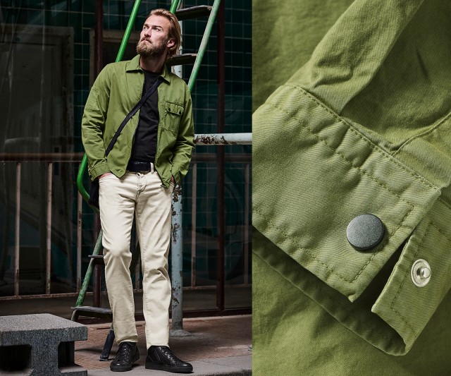 Das Bild zeigt einen Mann in einer hellen Hose, schwarzem Shirt und grüner Jacke, der vor einem Industrie-Hintergrund steht; daneben ist eine Detailaufnahme der grünen Jacke mit einem Druckknopf zu sehen.
