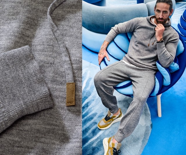 Ein Mann trägt ein graues, gemütliches Kapuzensweatshirt mit passender grauer Jogpants und sportlichen Sneakern in Beige‑Gelb‑Tönen.