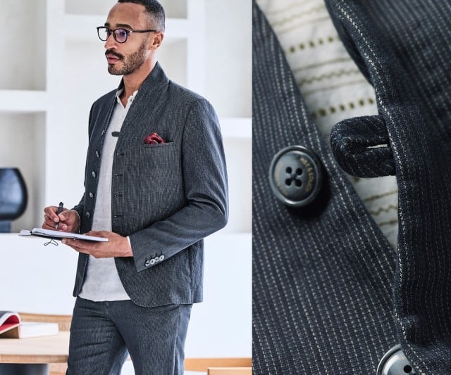 Ein Mann trägt einen fein strukturierten, dunkelgrauen Anzug im modernen Stehkragen‑Stil, kombiniert mit einem weißen Shirt und rotem Einstecktuch.