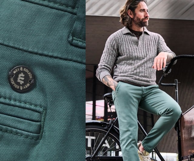 Ein Mann trägt einen grauen, grob gerippten Strickpullover mit offenem Polokragen zu einer grünen Chinohose und hellen Sneakern.