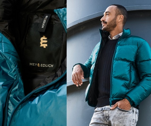 Auf dem Bild sieht man einen Mann bekleidet mit einer petrolfarbenen Steppjacke und einer grauen Jeans.