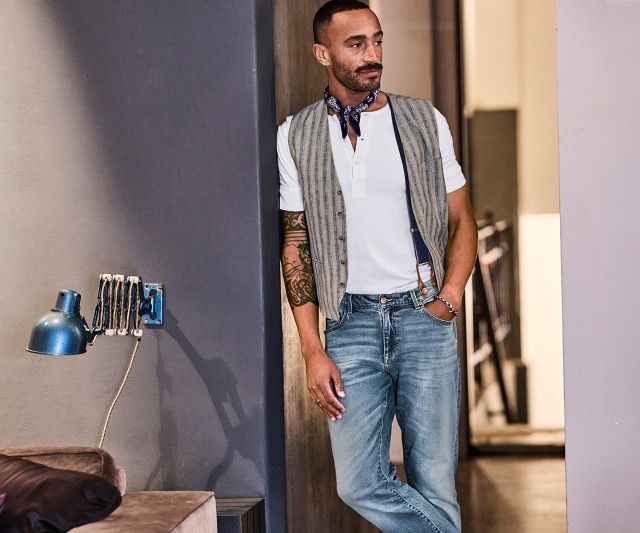 Mann in weißem Shirt mit gestreifter Weste und hellblauer Jeanshose